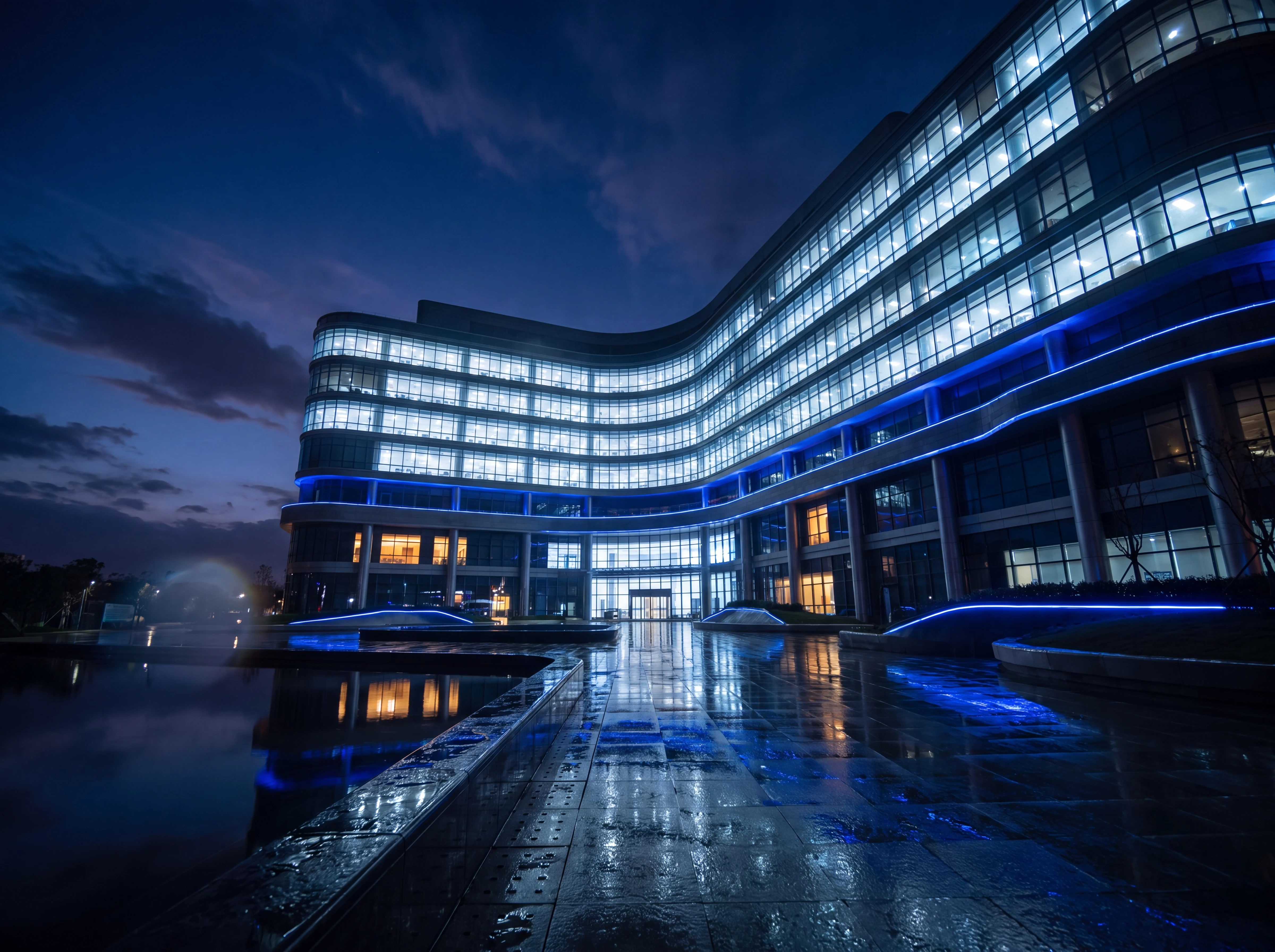 A modern multi-speciality hospital glowing at blue hour, mirrored in a wet forecourt
